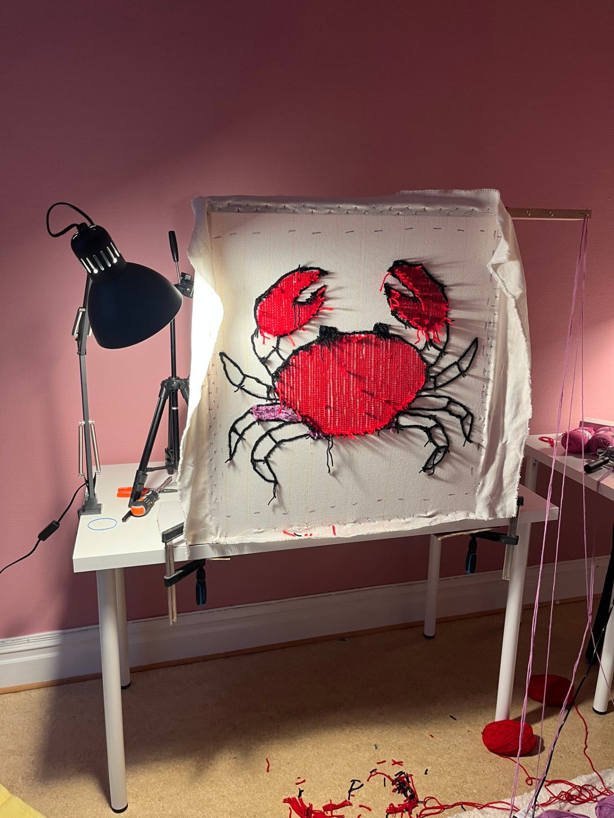 Tuftningsram med ett pågående motiv i ullipeys studio, med garn och verktyg på bordet